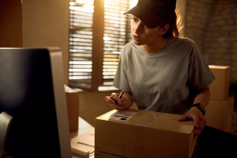 Profissional prepara pacotes de pedidos no computador para entrega de e-commerce