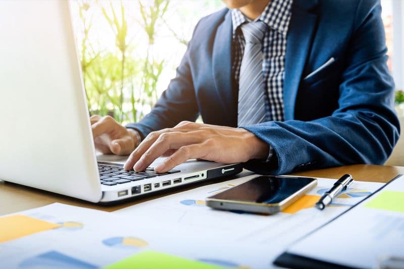 Empresário analisa gráficos financeiros e planilha de fluxo de caixa em um notebook sobre a mesa