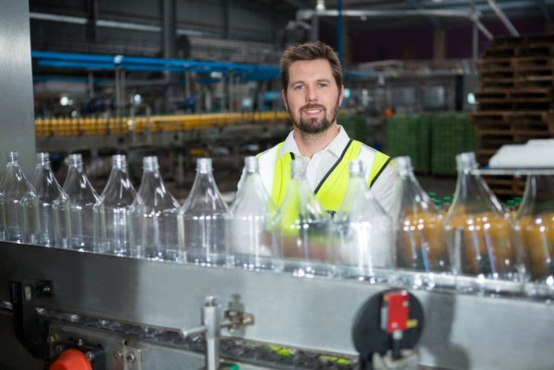 Trabalhador ao lado de uma linha de produção de bebidas em fábrica, setor afetado pelo Imposto Seletivo