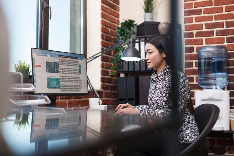 Contadora analisa dados em telas com gráficos enquanto usa um software com recursos de inteligência artificial