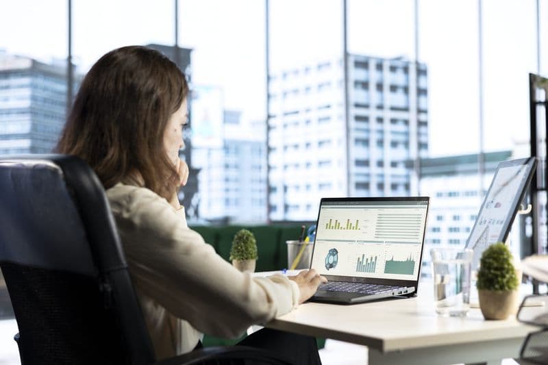 Profissional analisa gráficos financeiros no notebook em escritório com vista para a cidade